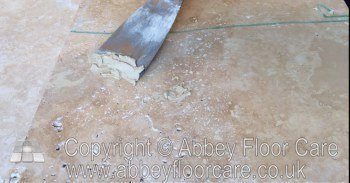 Grout filler being pressed into holes in travertine with a scraper